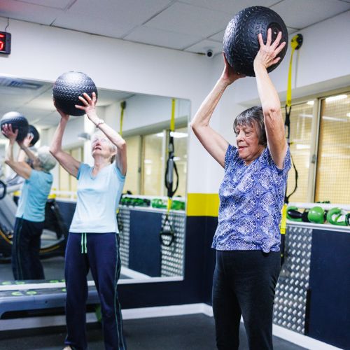 two senior ladies using slam balls in the gym