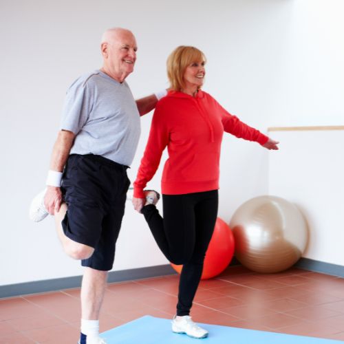 senior man and woman standing on one leg on a yoga mat